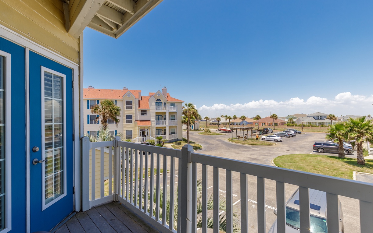 Bright coastal vacation rental with covered balcony overlooking tropical palms and resort community. Clear blue skies frame this relaxing beachside retreat.