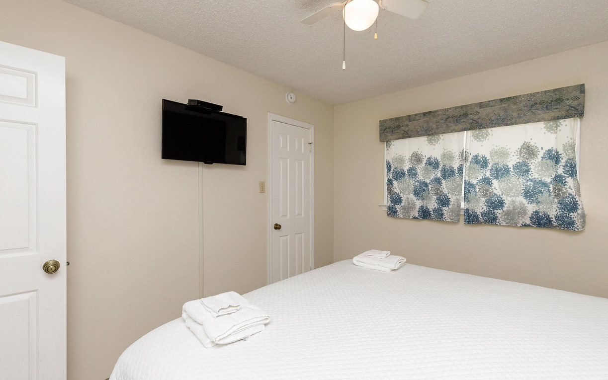 Unwind in your peaceful bedroom with crisp linens, wall-mounted TV, and gentle ceiling fan for your comfort.