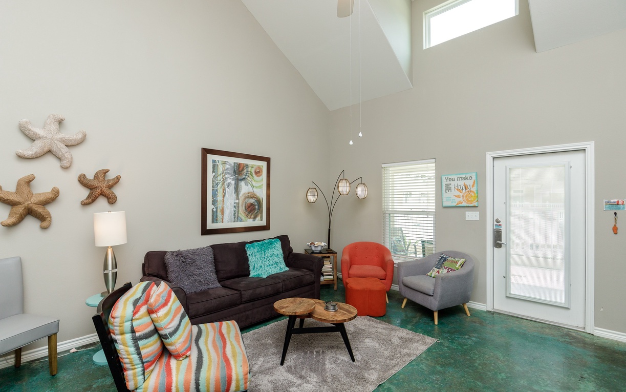 Unwind in your bright living room with soaring vaulted ceilings, colorful coastal decor, and comfortable seating perfect for relaxing after beach adventures.