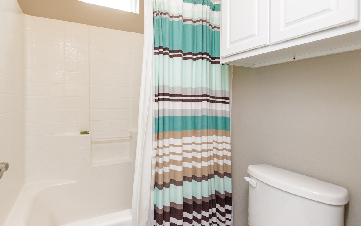 Your private bathroom features a refreshing tub-shower combo with cheerful striped curtains and convenient storage above.