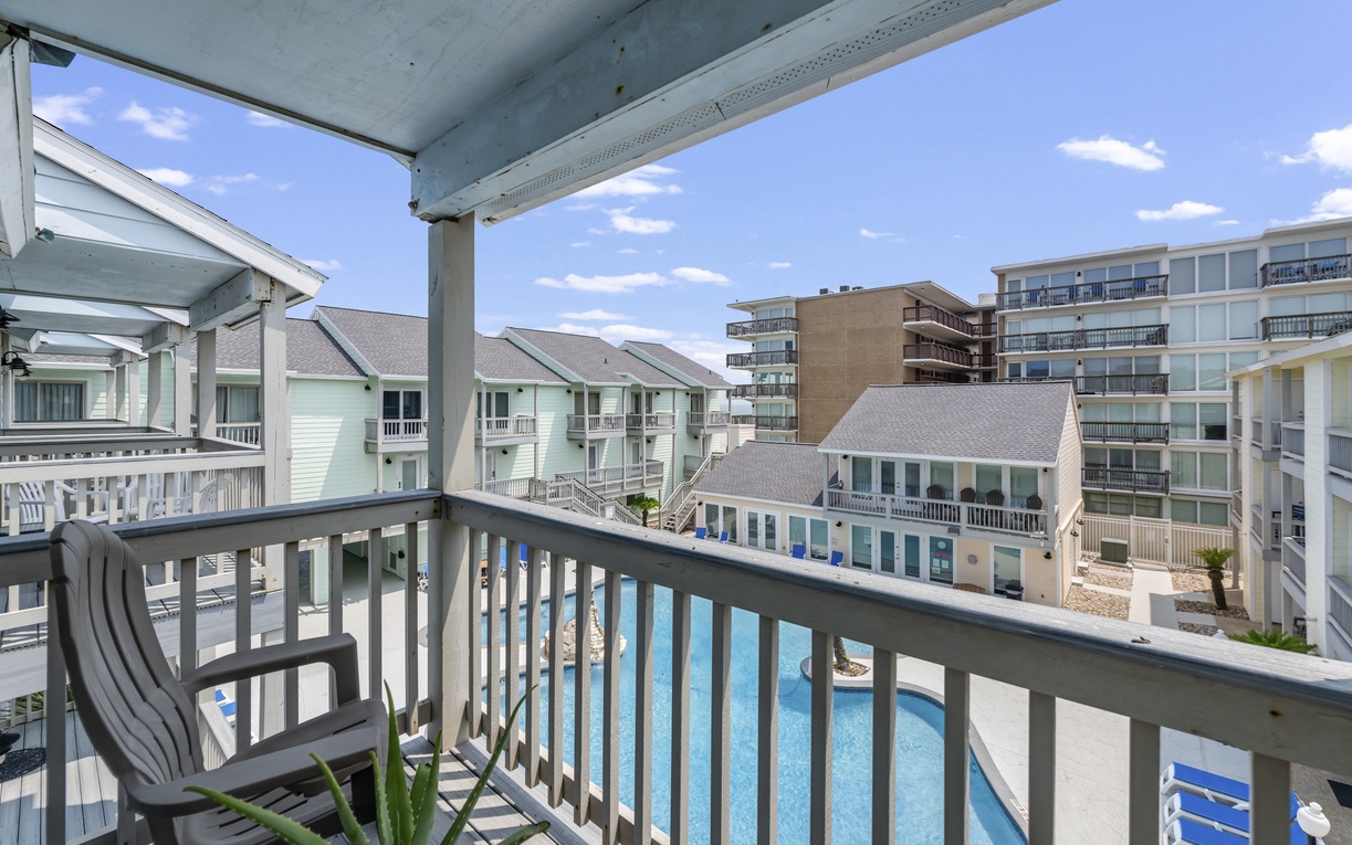 A covered balcony overlooks a sparkling pool and coastal property, with seating to enjoy the ocean breeze and sun-drenched surroundings.
