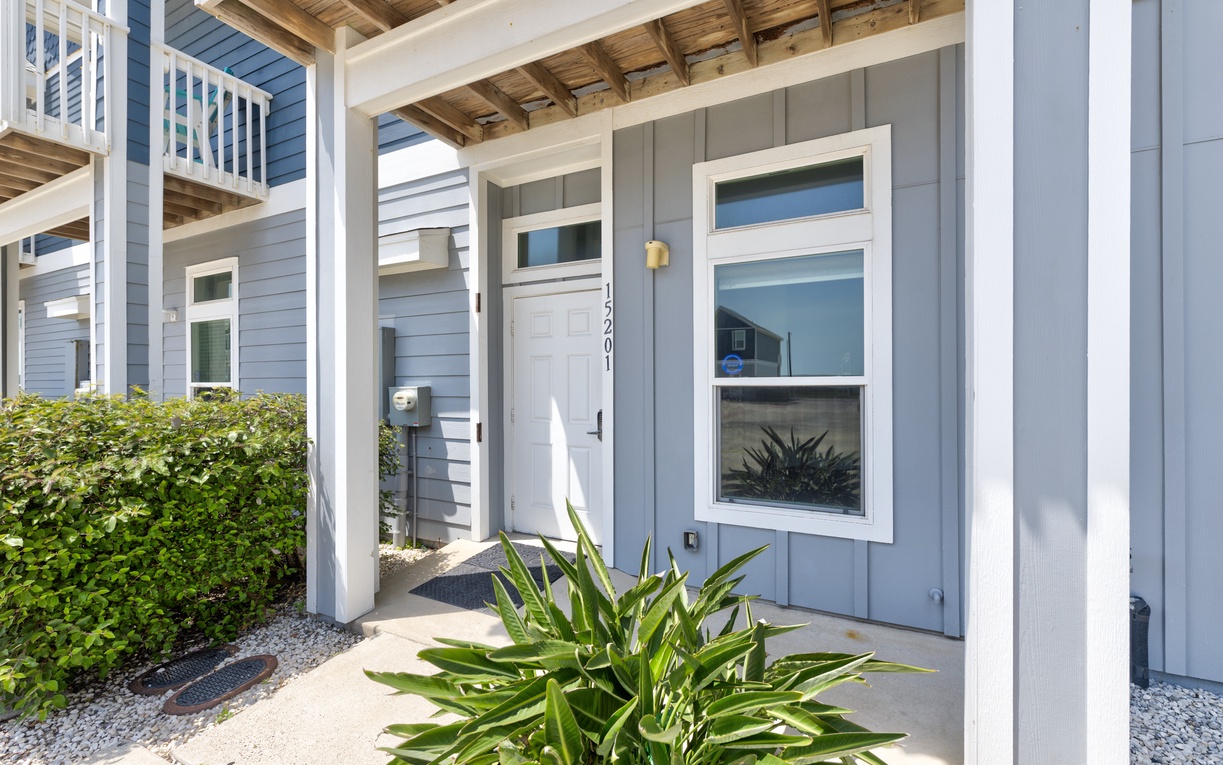 Contemporary blue exterior with white trim creates a welcoming entrance amid landscaped greenery and modern architectural details.