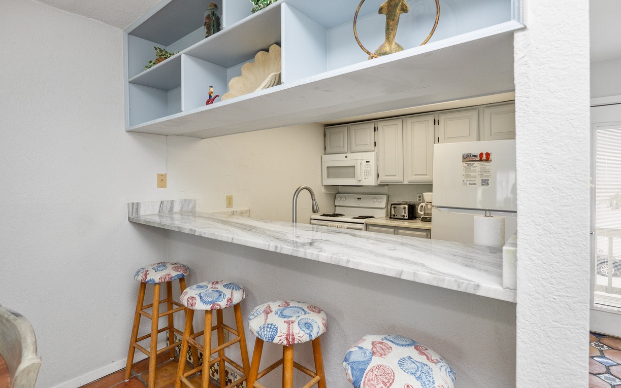 Your fully equipped kitchen features a breakfast bar with coastal-themed seating, perfect for morning coffee or casual dining together.