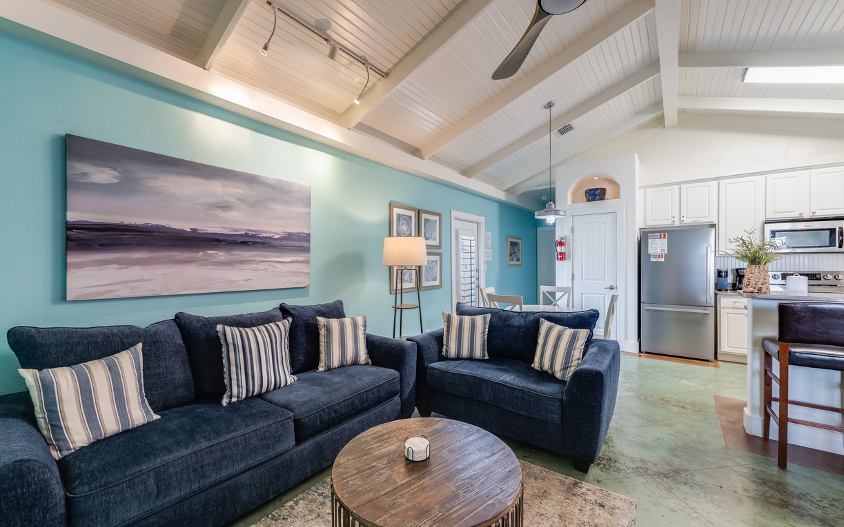 Sink into plush navy sofas beneath soaring white beams while you unwind in this bright, coastal-inspired living space.