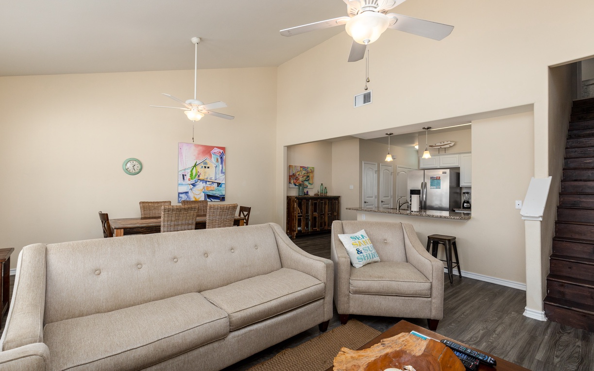 Relax in your spacious open-concept living area with comfortable seating, ceiling fans, and seamless flow to the fully equipped kitchen.