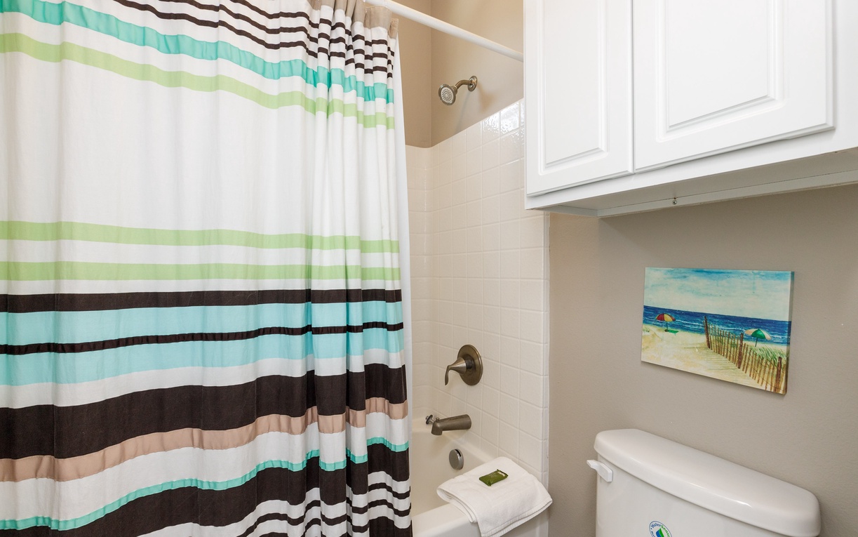 Step into your bright bathroom with colorful striped shower curtain and cheerful coastal artwork setting a relaxing seaside mood.