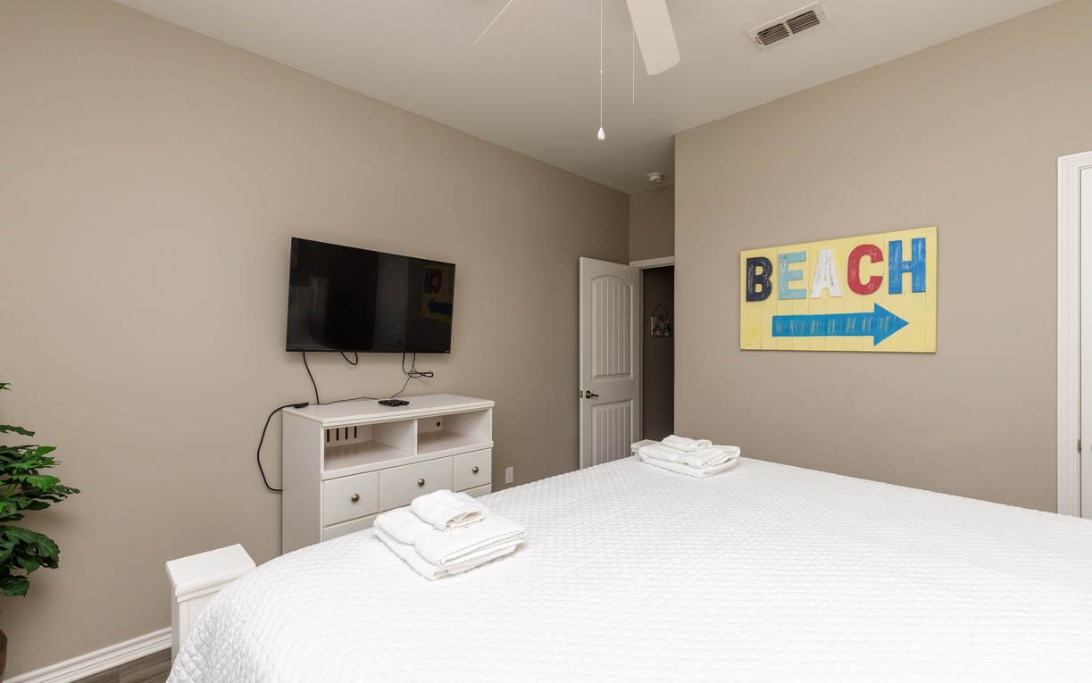 Unwind in your peaceful bedroom with crisp white linens, modern entertainment, and cheerful beach-themed decor to set the perfect vacation mood.