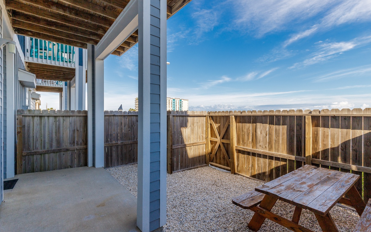 Your private patio features a rustic wooden table perfect for morning coffee under the covered pergola, surrounded by a charming wooden fence.