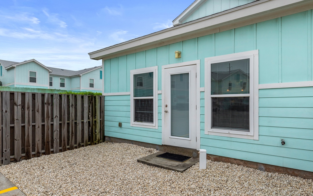 Charming turquoise cottage with private patio featuring gravel flooring and wooden fence for peaceful outdoor moments.