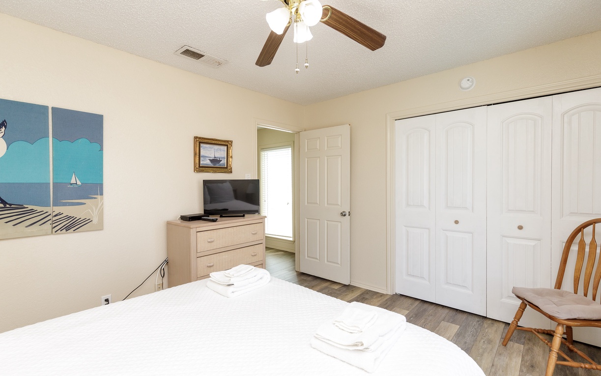 Your peaceful bedroom features coastal artwork, ceiling fan, TV, and generous closet space for a comfortable stay.