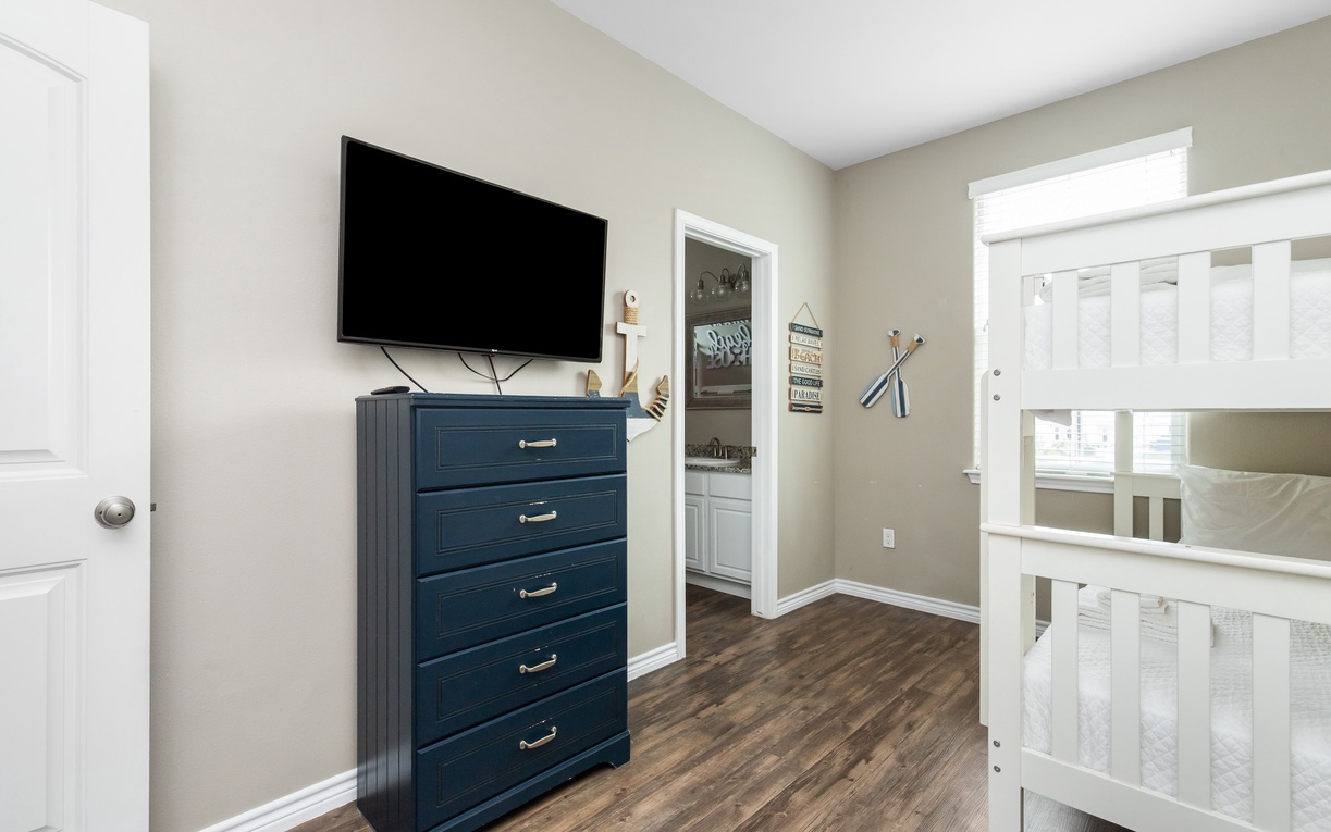 Your cozy bedroom features a wall-mounted TV and stylish navy dresser, perfect for relaxing after your adventures.