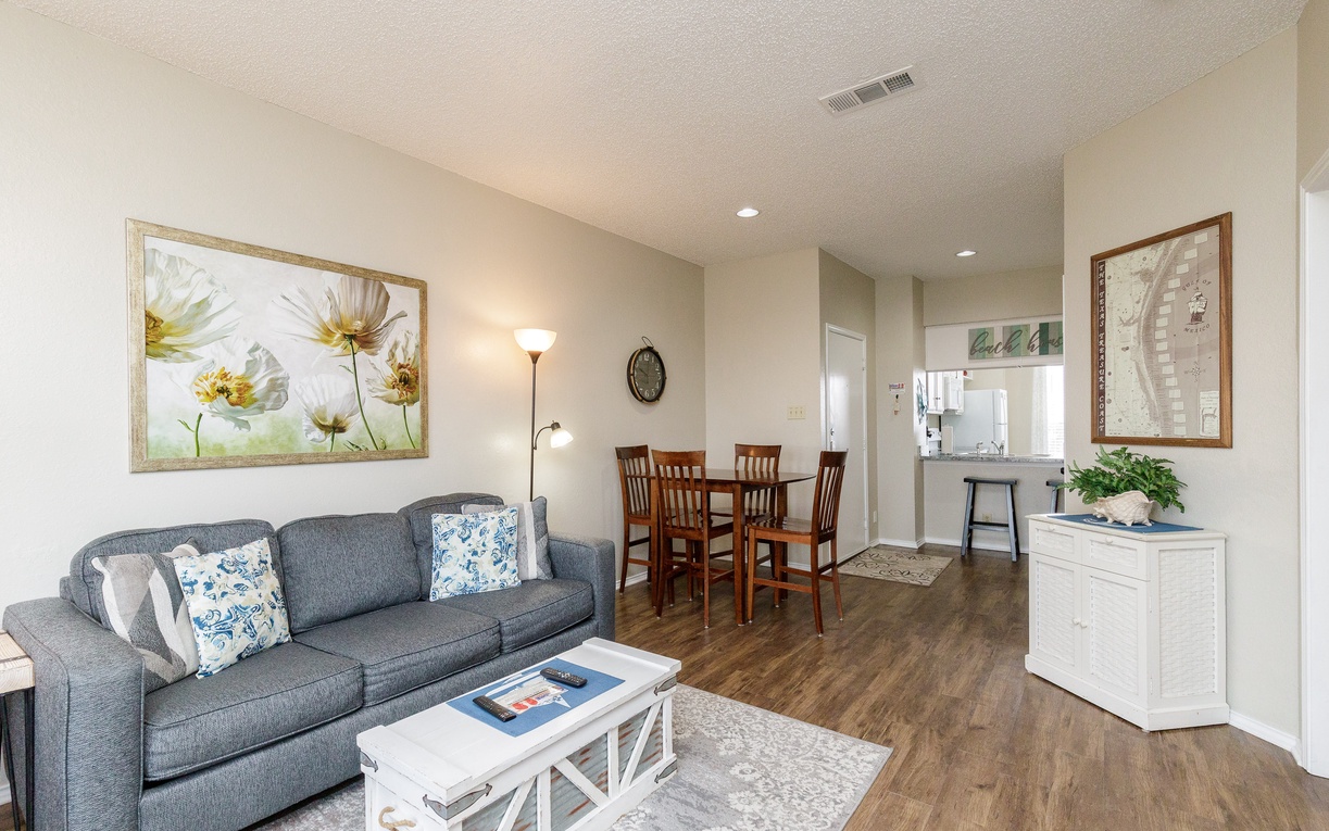 Relax in your bright, open living space featuring a cozy gray sofa, elegant dining area, and thoughtful touches like fresh flowers and local artwork.