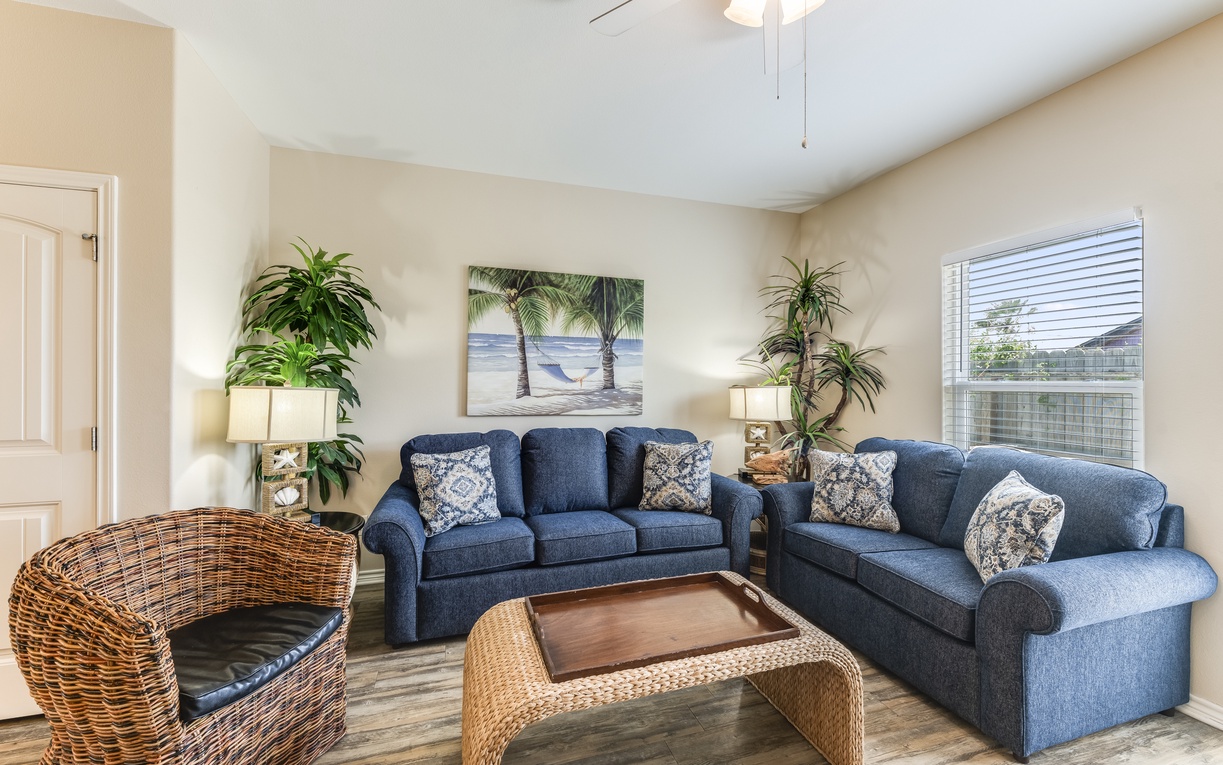 Relax in your coastal-themed living room with plush blue sofas and tropical art, perfect for unwinding after beach adventures.