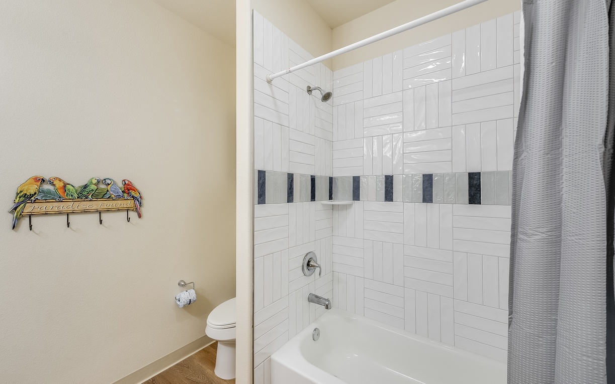 Your private bathroom features a bright white tiled shower-tub combo with cheerful tropical parrot artwork welcoming you home.
