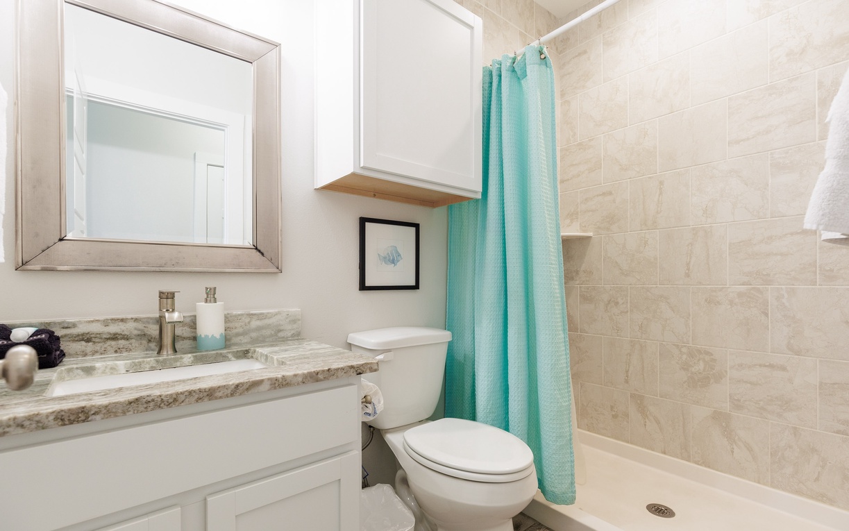 Step into your private bathroom featuring marble countertops, modern fixtures, and a relaxing tiled shower with cheerful turquoise curtains.