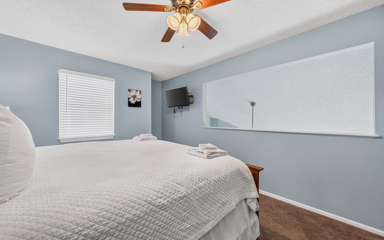 Your peaceful retreat features calming blue walls, a ceiling fan for comfort, and fresh towels waiting at the foot of your bed—ready for restful nights.