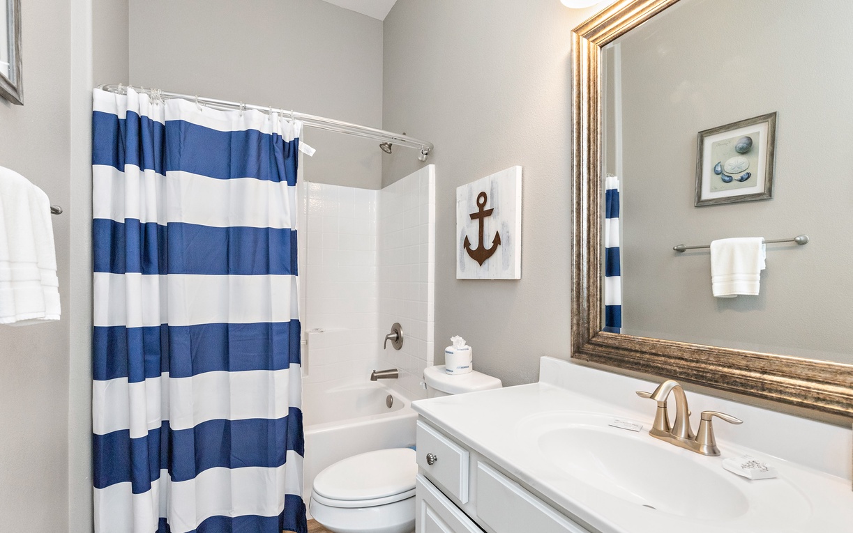 Refresh in your charming nautical-themed bathroom, complete with blue striped curtains and coastal artwork for seaside serenity.