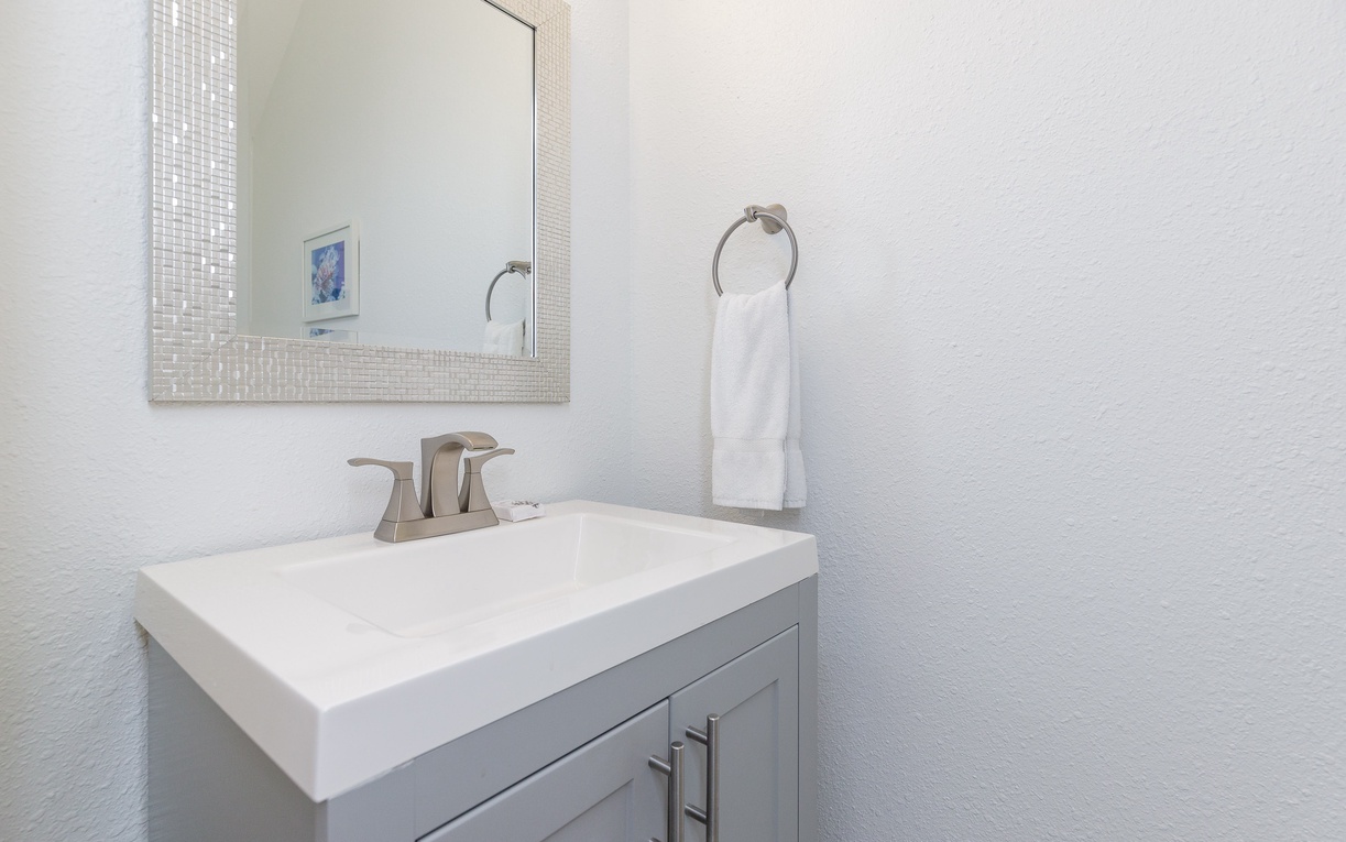 Refresh in your pristine powder room with modern finishes, elegant mosaic-framed mirror, and thoughtfully placed towels for your comfort.