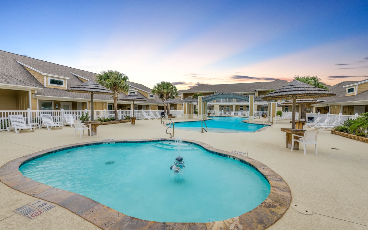 A peaceful resort pool area with palm trees and multiple swimming pools under a beautiful twilight sky.