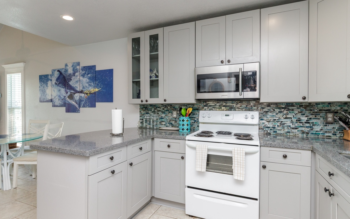 Whip up your favorite meals in this bright, fully-equipped kitchen featuring granite countertops, modern appliances, and ocean-inspired tile backsplash.