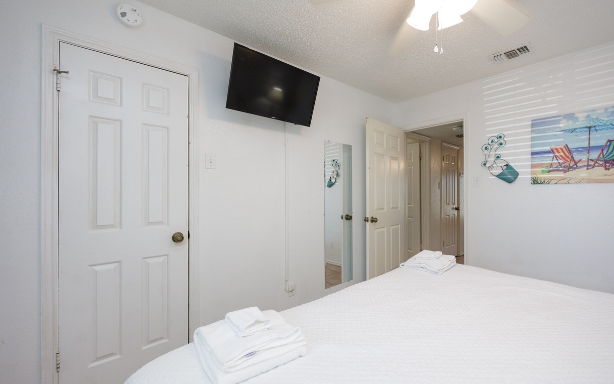 Unwind in your bright bedroom with wall-mounted TV, crisp linens, and cheerful beach artwork creating a peaceful retreat.