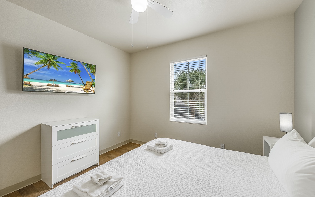 Relax in your peaceful bedroom with crisp white linens, tropical wall art, and natural light streaming through your window.