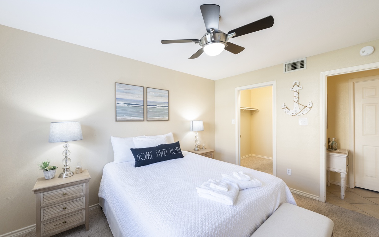 Sink into crisp white linens in your peaceful bedroom retreat, complete with coastal artwork and gentle ceiling fan breeze.