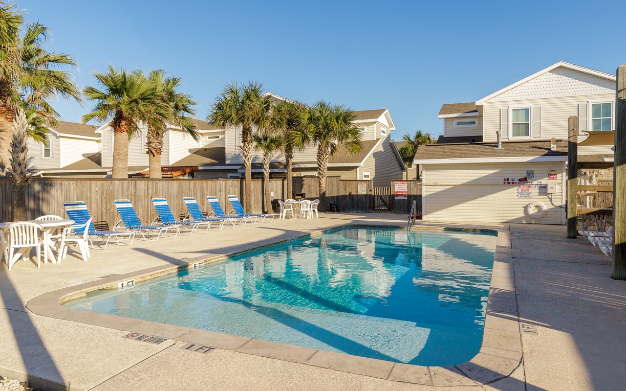 Coastal vacation rental community featuring a sparkling swimming pool surrounded by palm trees and comfortable beach-style homes.