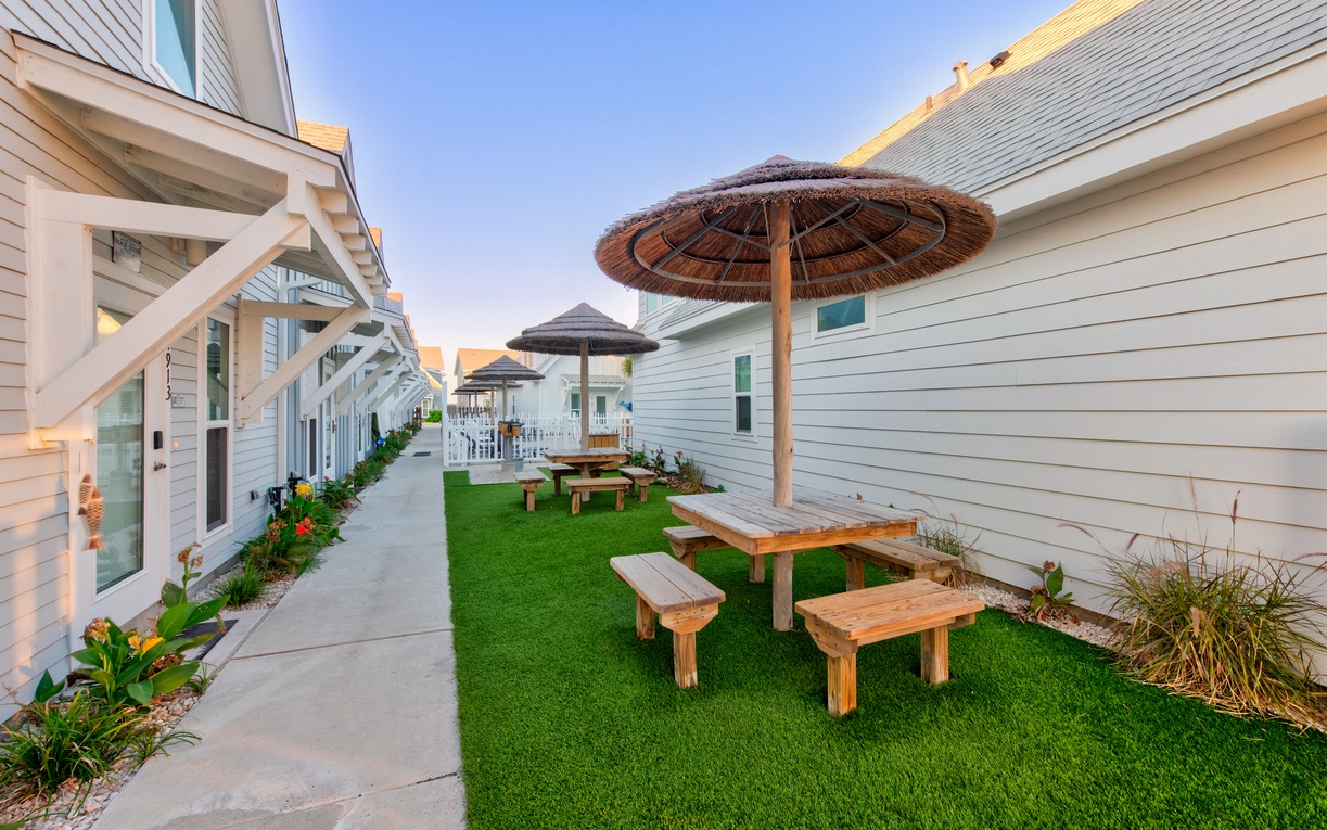 Charming beach-style property features wooden picnic tables under thatched umbrellas, creating perfect spots for outdoor dining and relaxation.
