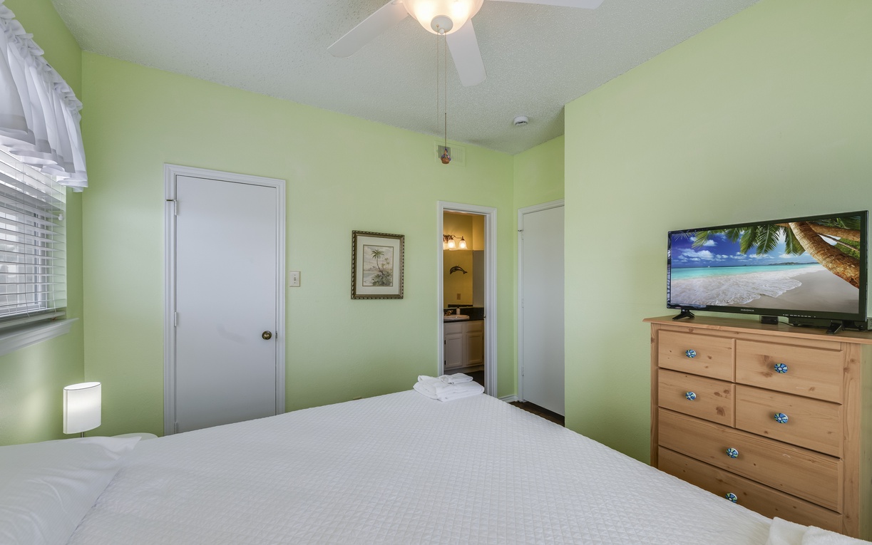 Another view of the guest bedroom showcasing a dresser with TV, ample storage, and convenient access to the nearby bathroom.