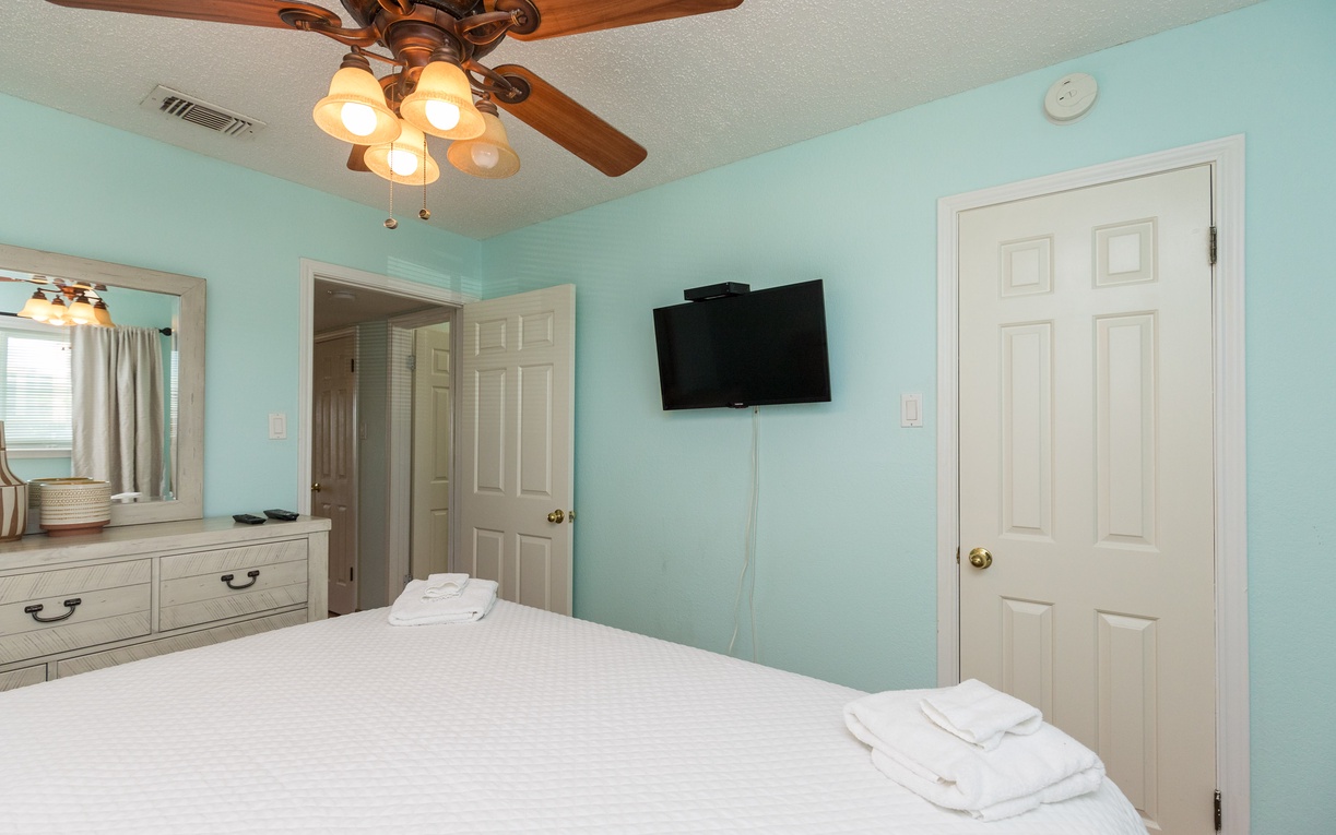 Your serene turquoise bedroom creates a peaceful retreat with crisp linens, vintage ceiling fan, and modern entertainment for ultimate comfort.