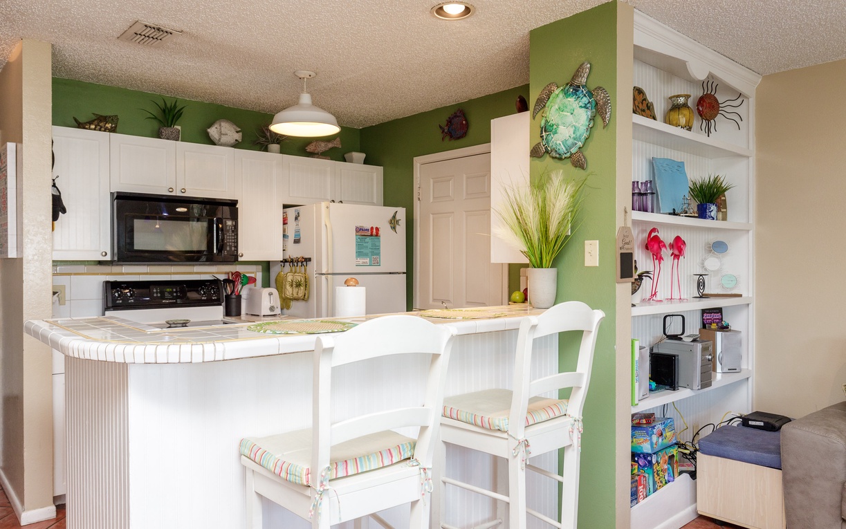 Your bright kitchen features cheerful green accents, white cabinetry, and a breakfast bar where you can enjoy morning coffee together.
