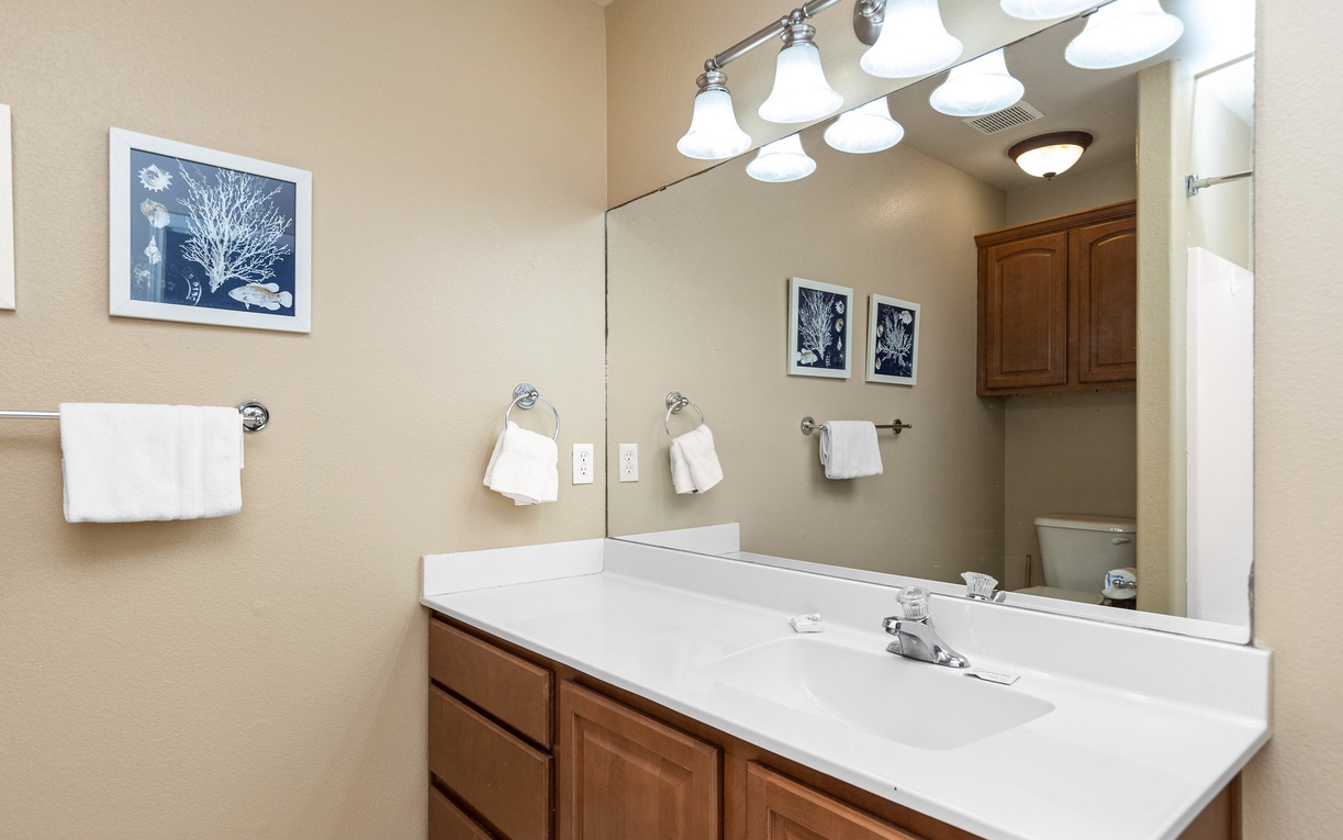 Your spacious bathroom features a long vanity with pristine white countertops, warm wood cabinetry, and thoughtful touches like coastal artwork to make you feel at home.