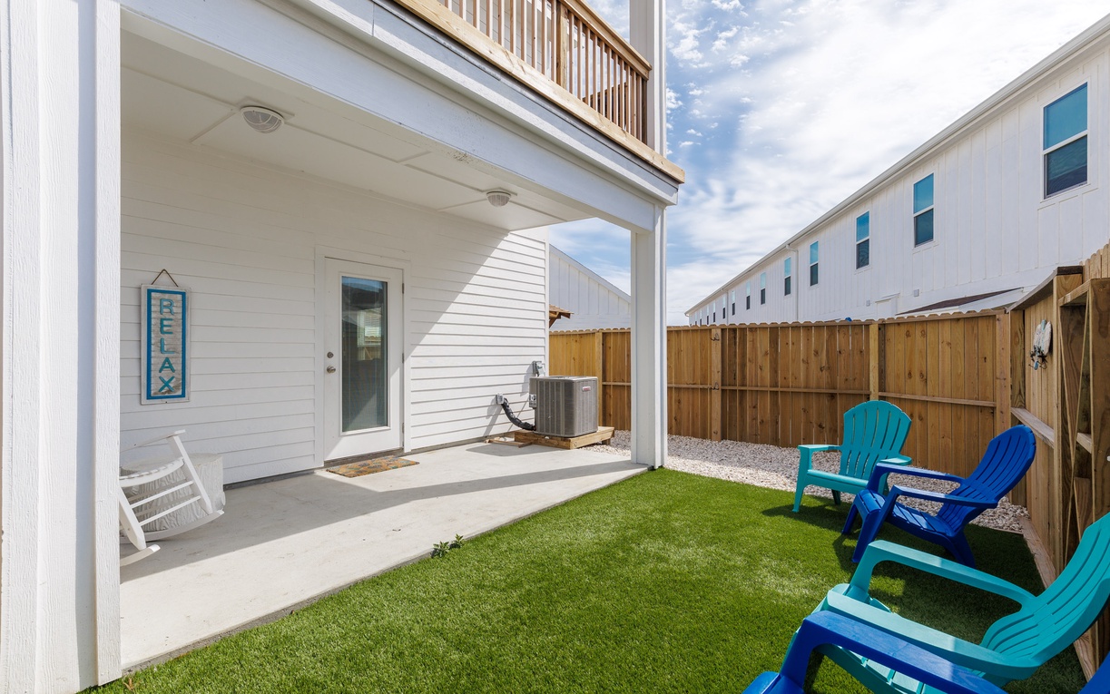 Your private backyard oasis features colorful Adirondack chairs on lush turf, perfect for morning coffee or evening relaxation.