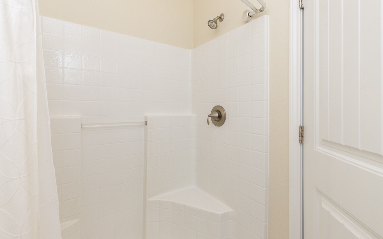 Step into your pristine walk-in shower with gleaming white tiles and modern fixtures for a refreshing start to your day.