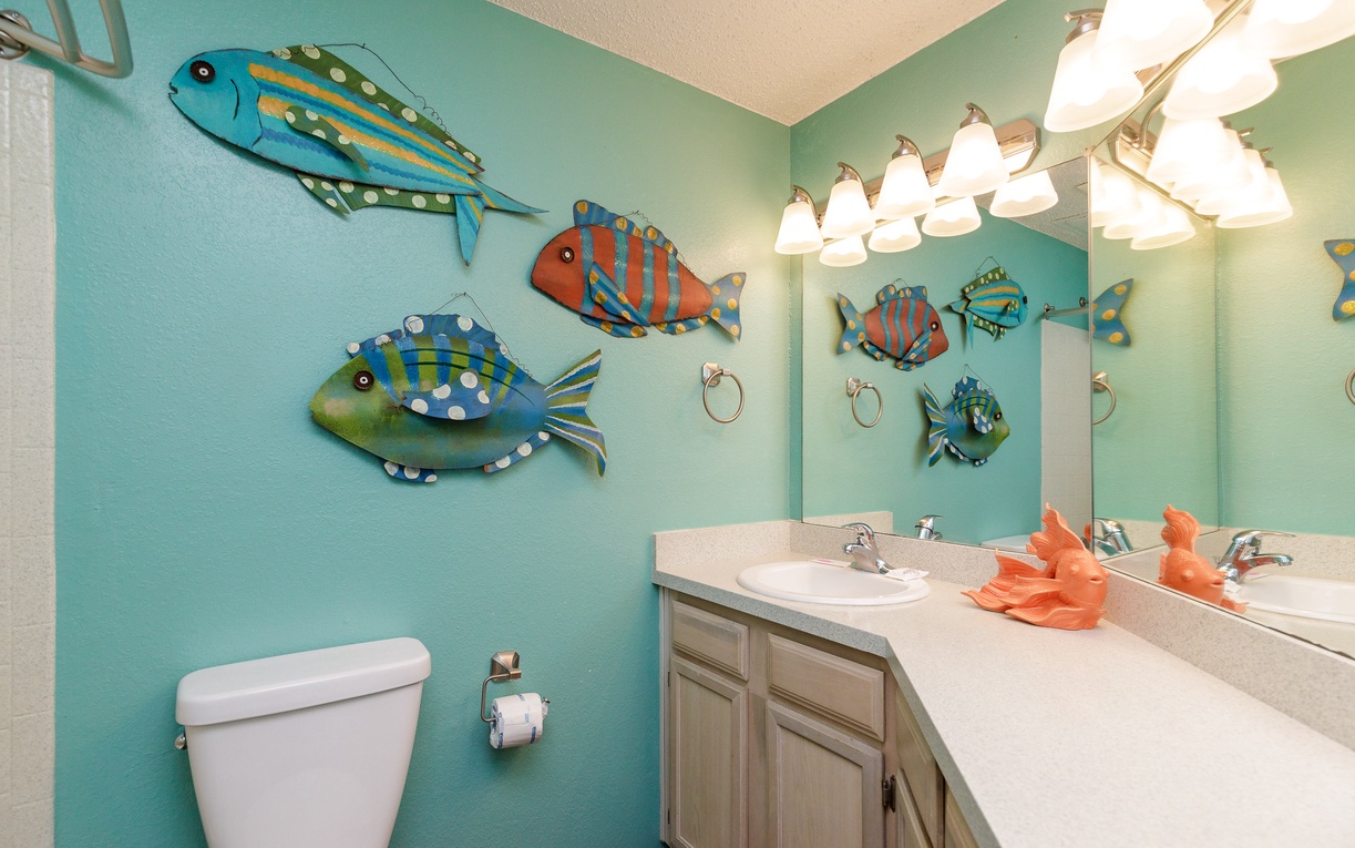 Dive into your own underwater paradise with whimsical fish art adorning aqua walls, bright vanity lighting, and cheerful coral towels.