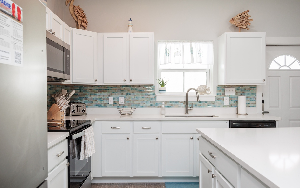 Step into your bright, fully-equipped kitchen with sparkling white countertops, coastal-inspired tile backsplash, and everything you need to create delicious meals during your stay.
