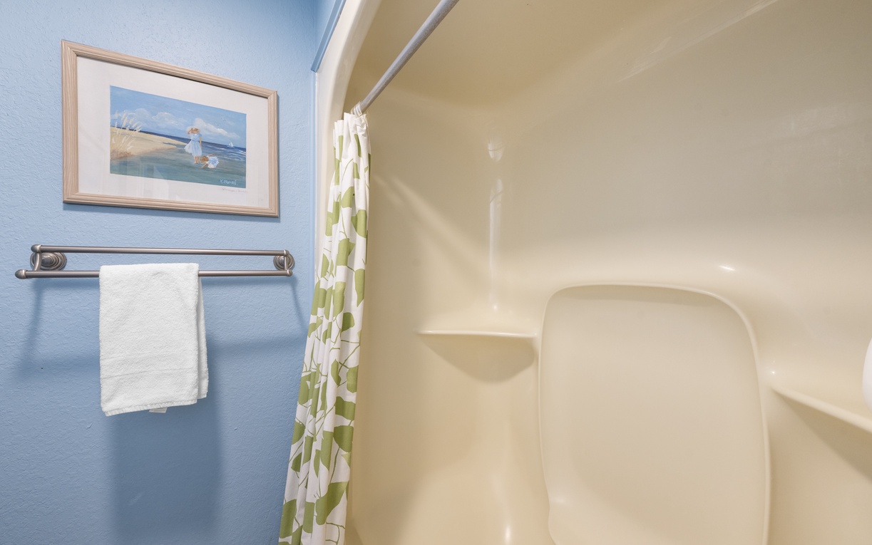 Step into your private bathroom featuring a spacious tub-shower combo, fresh towels, and cheerful coastal artwork.