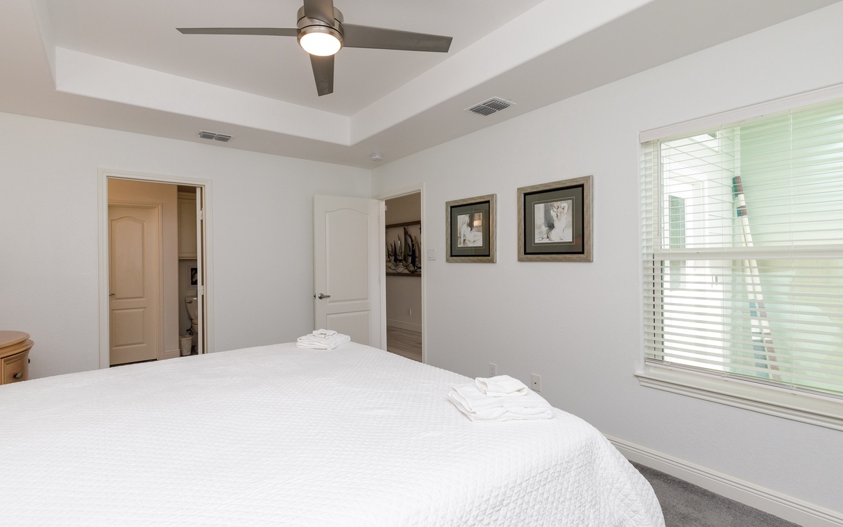 Rest peacefully in your bright, airy bedroom featuring crisp linens, elegant ceiling fan, and peaceful garden views through large windows.
