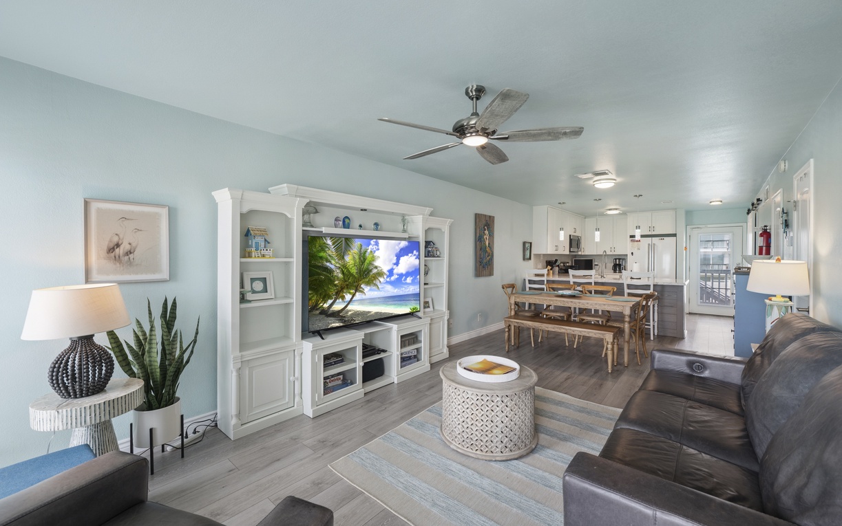 Relax in your open-concept living space featuring coastal décor, comfortable seating, and a ceiling fan. The full kitchen and dining area invite you to unwind after beach days.
