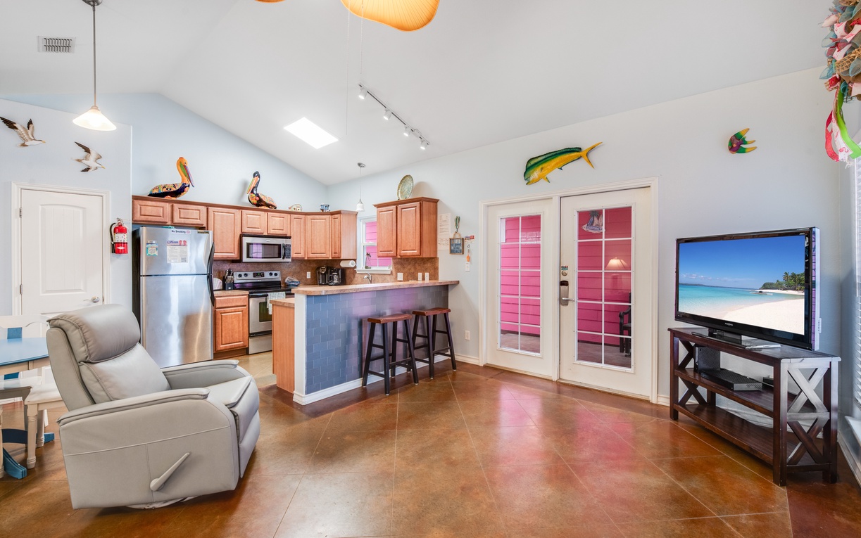 Relax in your bright, open-concept space where a fully equipped kitchen flows seamlessly into your comfortable living area with tropical beach scenes on the TV.