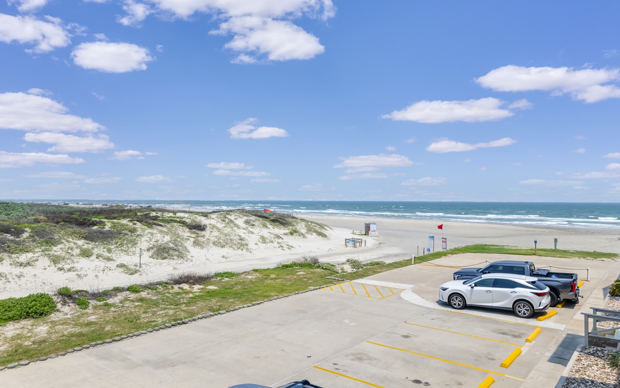 Coastal property features beachfront location with convenient parking overlooking sandy shores, dunes, and turquoise waters—just steps from the waves.