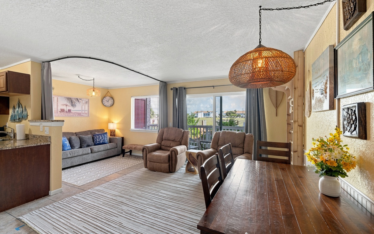 Relax in your open-concept living space with comfortable seating, a stylish woven pendant light, and water views just beyond the balcony—perfect for unwinding after a day of exploration.