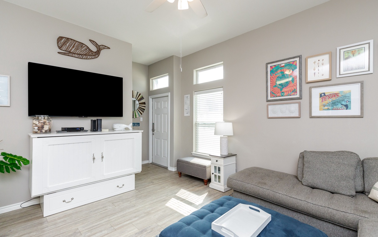 Unwind in your bright, coastal-inspired living space featuring a large smart TV and artwork-filled walls perfect for relaxing evenings.