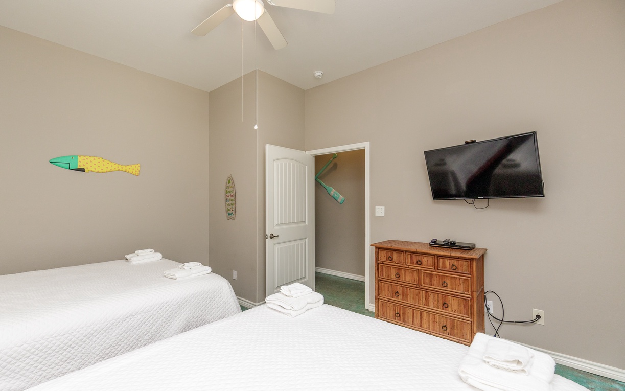Relax in your peaceful bedroom with two comfortable beds, ceiling fan, and entertainment center for cozy evenings.