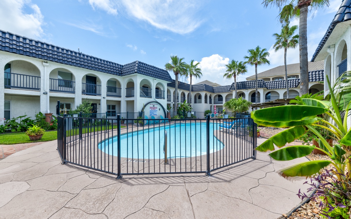 Mediterranean-style property features a sparkling pool surrounded by tropical palms and lush landscaping under beautiful blue skies.