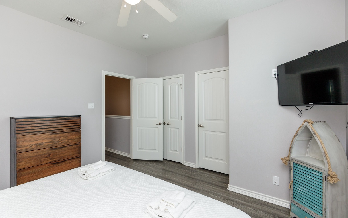 Relax in your serene bedroom featuring a ceiling fan for comfort, wall-mounted TV for entertainment, and charming nautical décor.