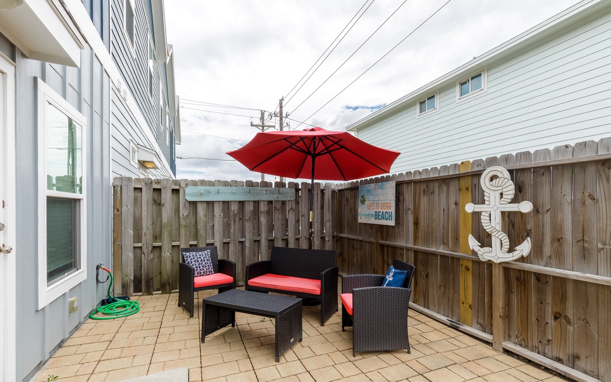 Step into your private patio where nautical charm meets comfort—relax on cushioned wicker furniture under your red umbrella.