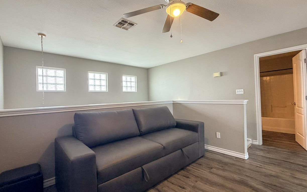 Relax in your private living space with modern furnishings, ceiling fan for comfort, and natural light from charming windows. The sleek sofa invites you to unwind after exploring.