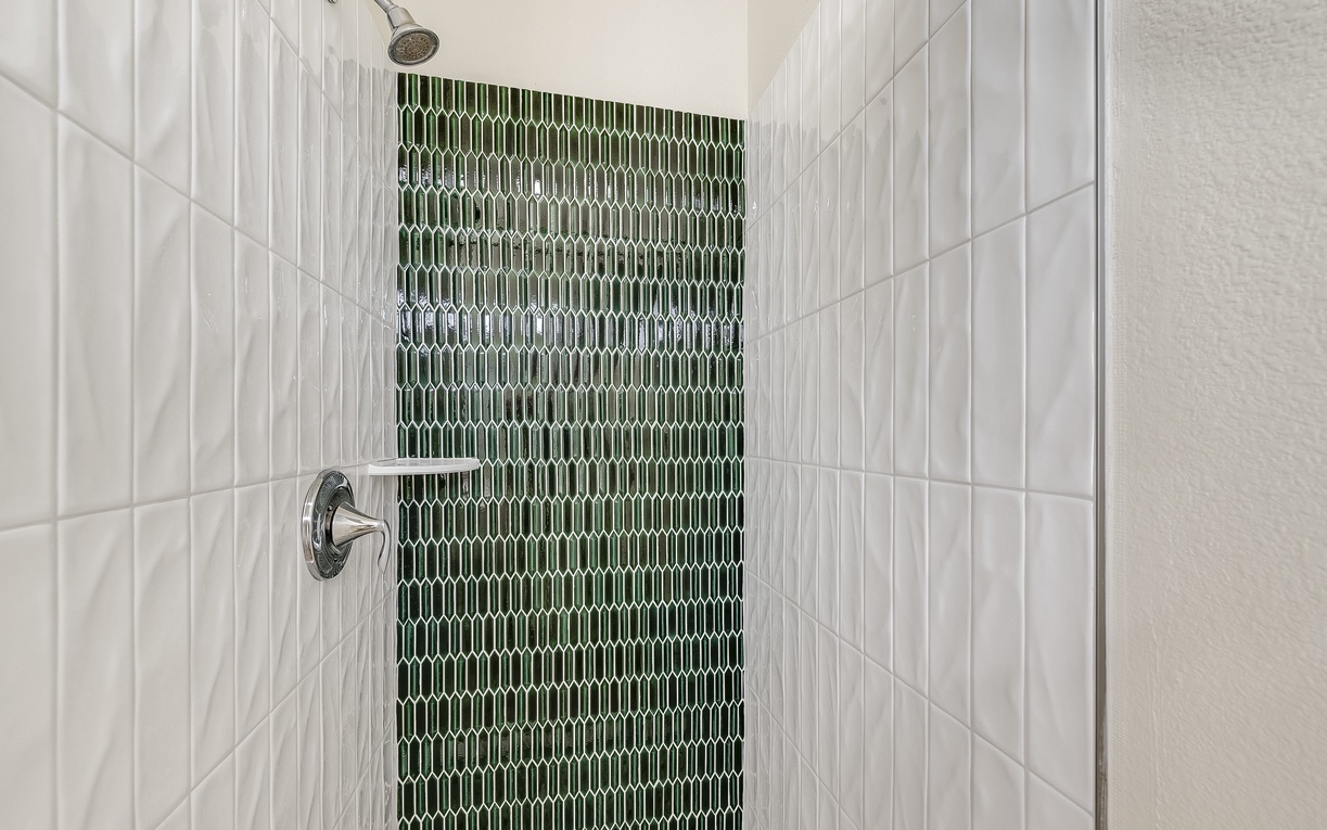 Step into your private shower oasis featuring stunning green mosaic tiles and refreshing rainfall overhead.